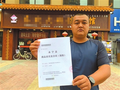 馬先生在自己的營(yíng)業(yè)房前向記者出示他的購(gòu)房合同。